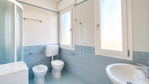 A bathroom with a toilet, bidet, and sink, with blue and white tiles and a window.