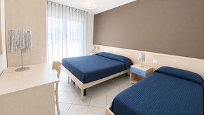 A hotel room with two beds, a desk, a chair, and a large window with curtains.