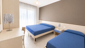A hotel room with two beds, a desk, a chair, a lamp, and a window with curtains.