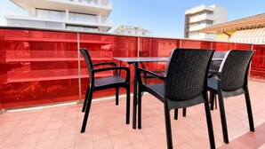 A rooftop terrace with a table and chairs, a red fence, and buildings in the background.