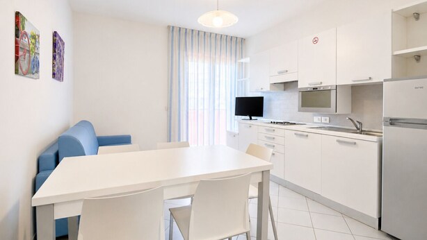 A modern kitchen with white cabinets, a dining table, and a blue sofa.