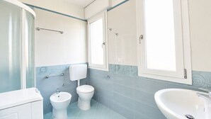 A bathroom with a shower, toilet, bidet, and sink.