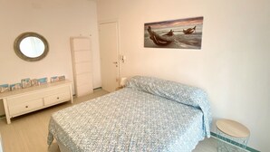 A bedroom with a bed, a dresser, a round mirror, a door, and a painting of a boat on the wall. - Appartamento Tarvisium - Carraro Immobiliare Jesolo (Lido di Jesolo)