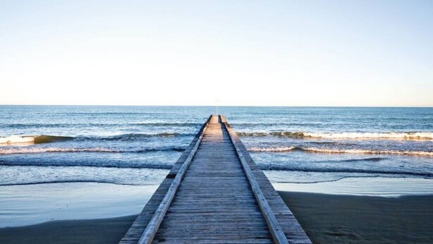 A wooden pier extending into the ocean with waves lapping at its ends. - Appartamento Tarvisium - Carraro Immobiliare Jesolo (Lido di Jesolo)