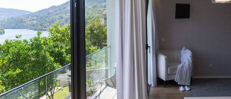 Una habitación moderna con un amplio ventanal que da a un balcón con vistas a un lago y colinas.
