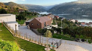 A modern house with a large patio, surrounded by lush greenery and a scenic lake view. - Portovella (Baiao)