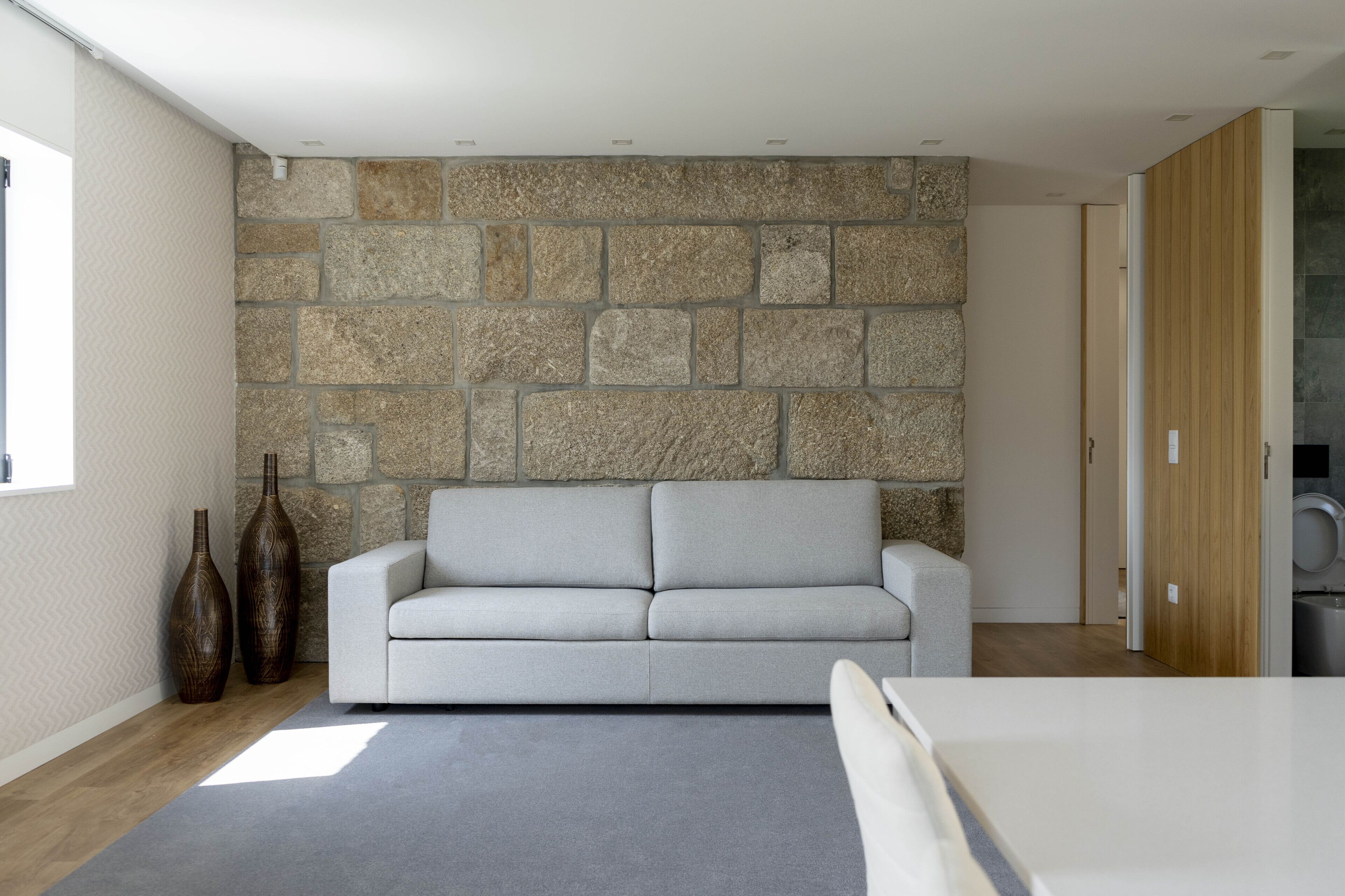 Una sala de estar moderna con una pared de piedra, un sofá de gris claro y dos jarrones decorativos.
