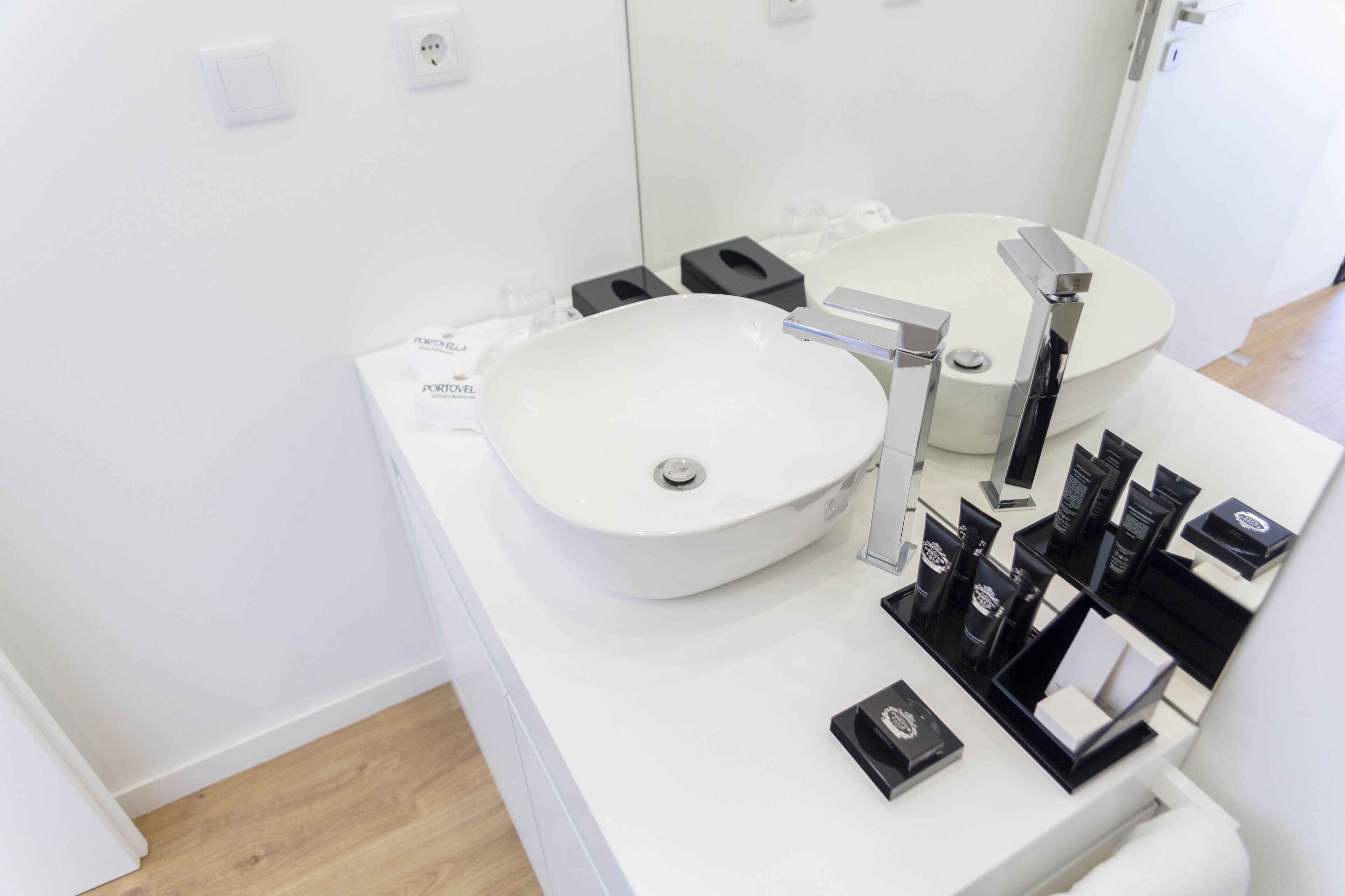 A modern bathroom with a white sink, two mirrors, and a black soap dispenser on the counter.
