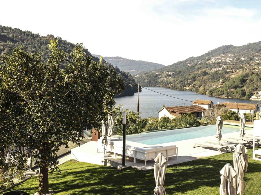 A pool area with lounge chairs and umbrellas, surrounded by a lush green lawn and a view of a lake and hills.