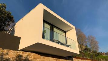 Una casa moderna con techo plano, un balcón con barandilla de vidrio y base de pared de piedra.