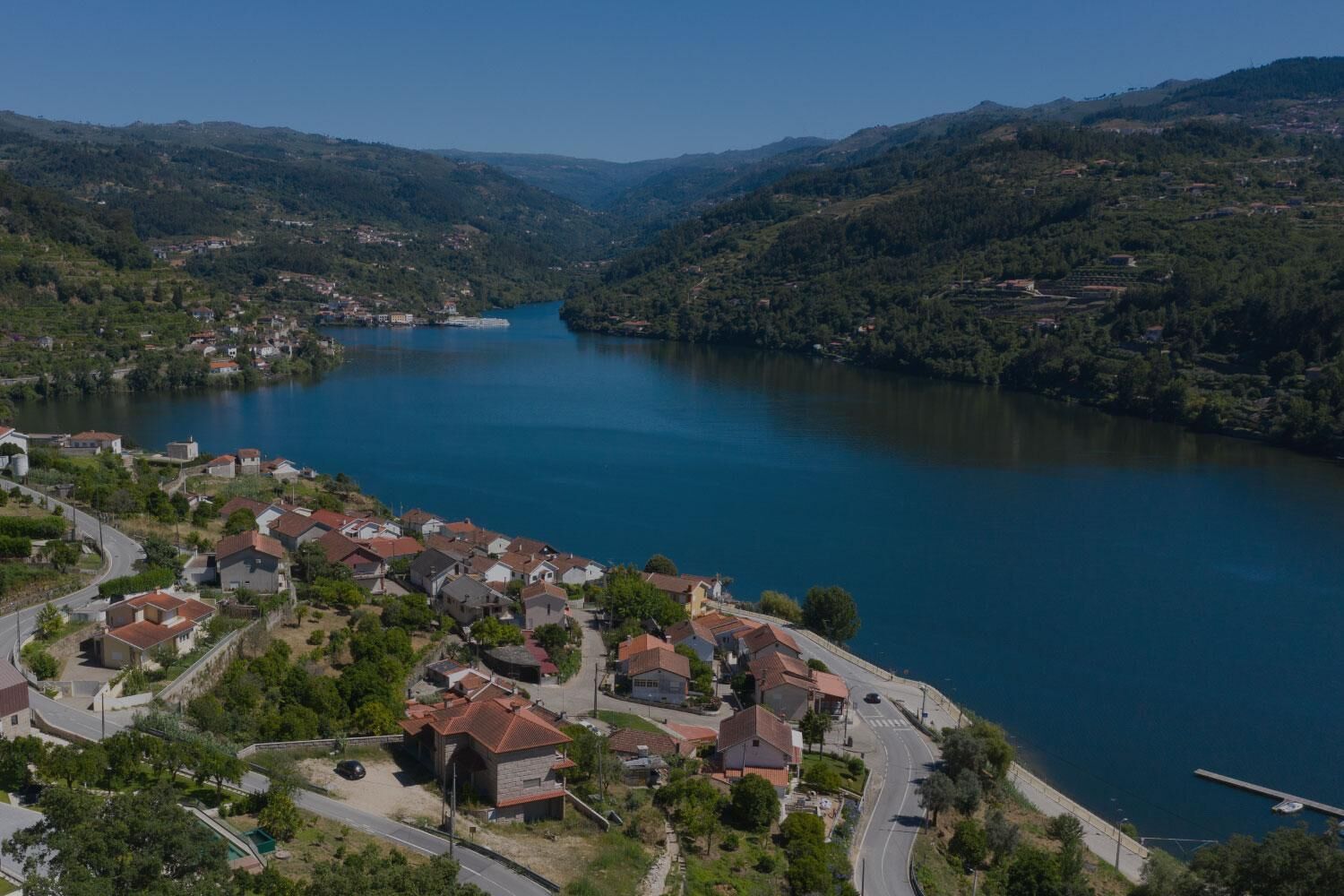 Un'area residenziale con case lungo la riva, una strada e un corso d'acqua circondato da colline.