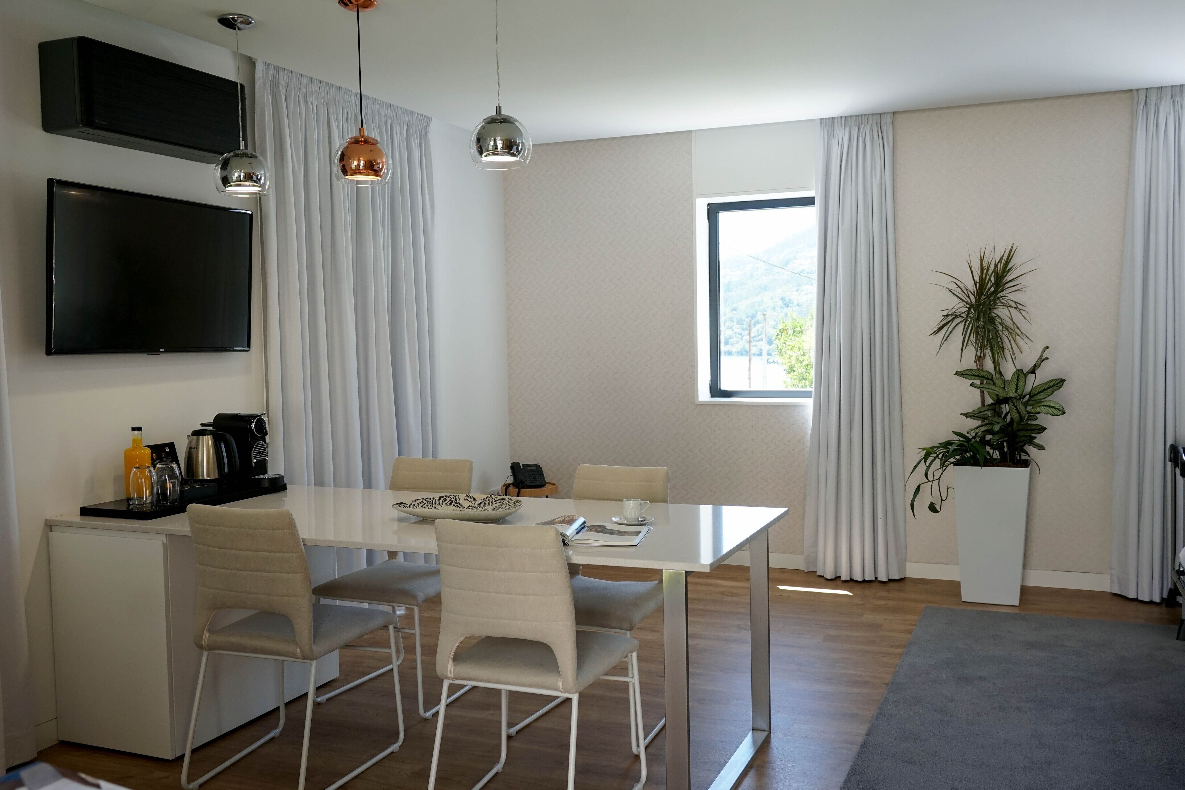 A modern dining area with a white table, four chairs, a flat-screen TV, and a coffee machine.
