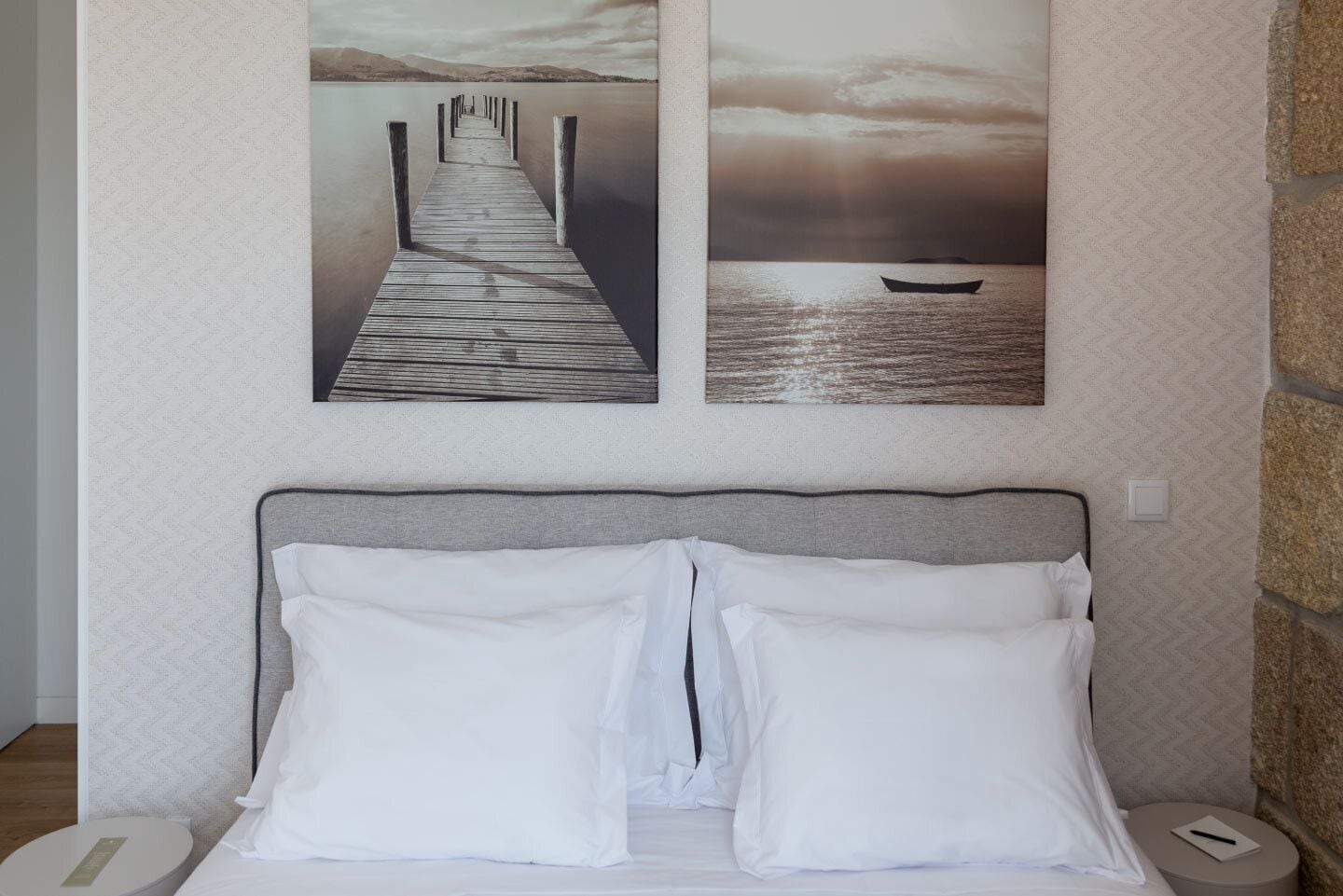Un dormitorio con cama, almohadas, cabecera y una obra de arte en la pared que muestra un muelle y un bote.