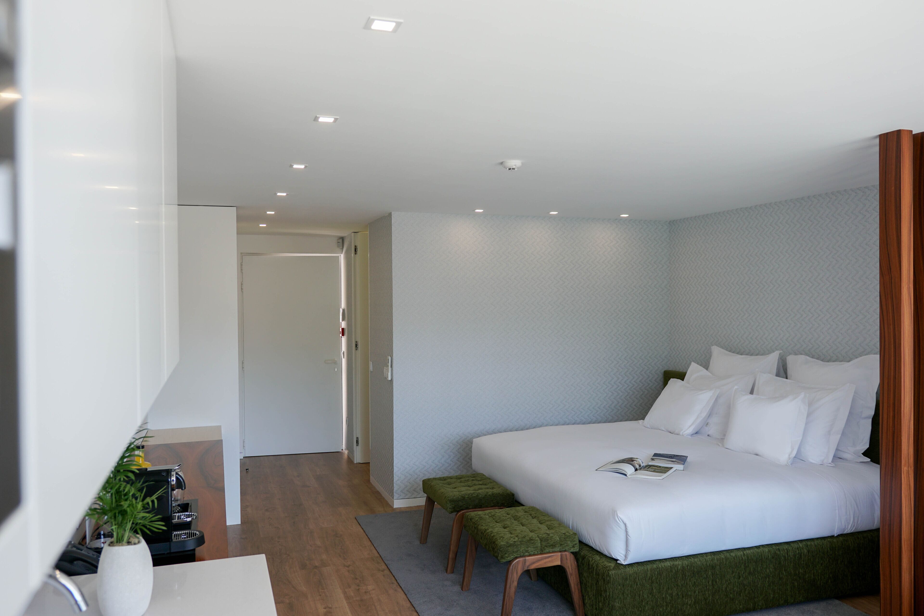 A modern hotel room with a large bed, a small seating area, and a bathroom visible through an open door.
