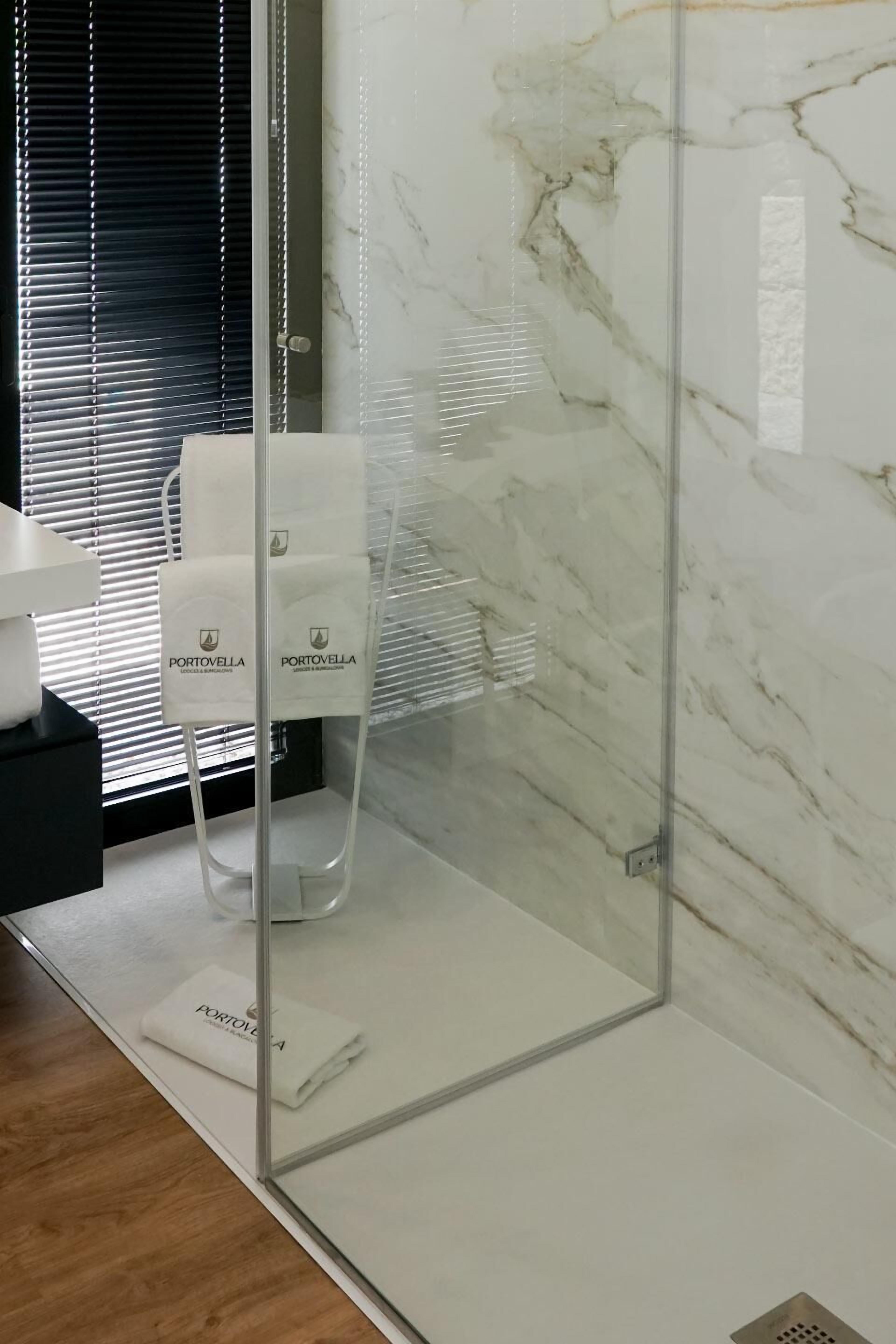 Un bagno con cabina doccia in vetro, pareti in marmo bianco e un piano d'appoggio nero.