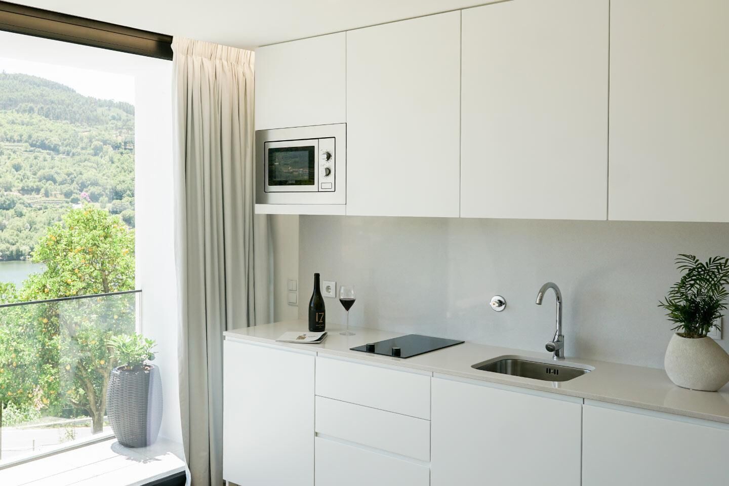 Una cocina moderna con microondas incorporado, una botella de vino y una copa de vino tinto sobre la encimera.