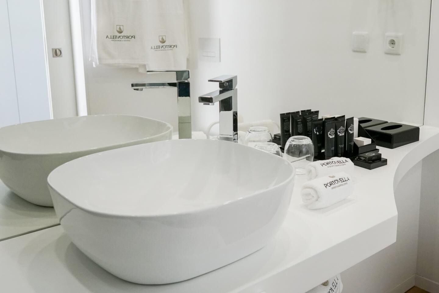 Un baño moderno con dos lavabos grandes blancos, un espejo y artículos de aseo en la encimera.