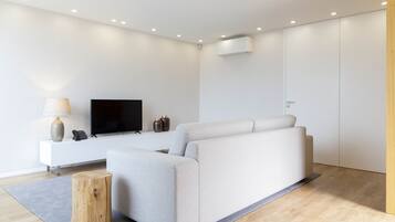 A modern living room with a sofa, a flat-screen TV, a small side table, and a wooden stool.