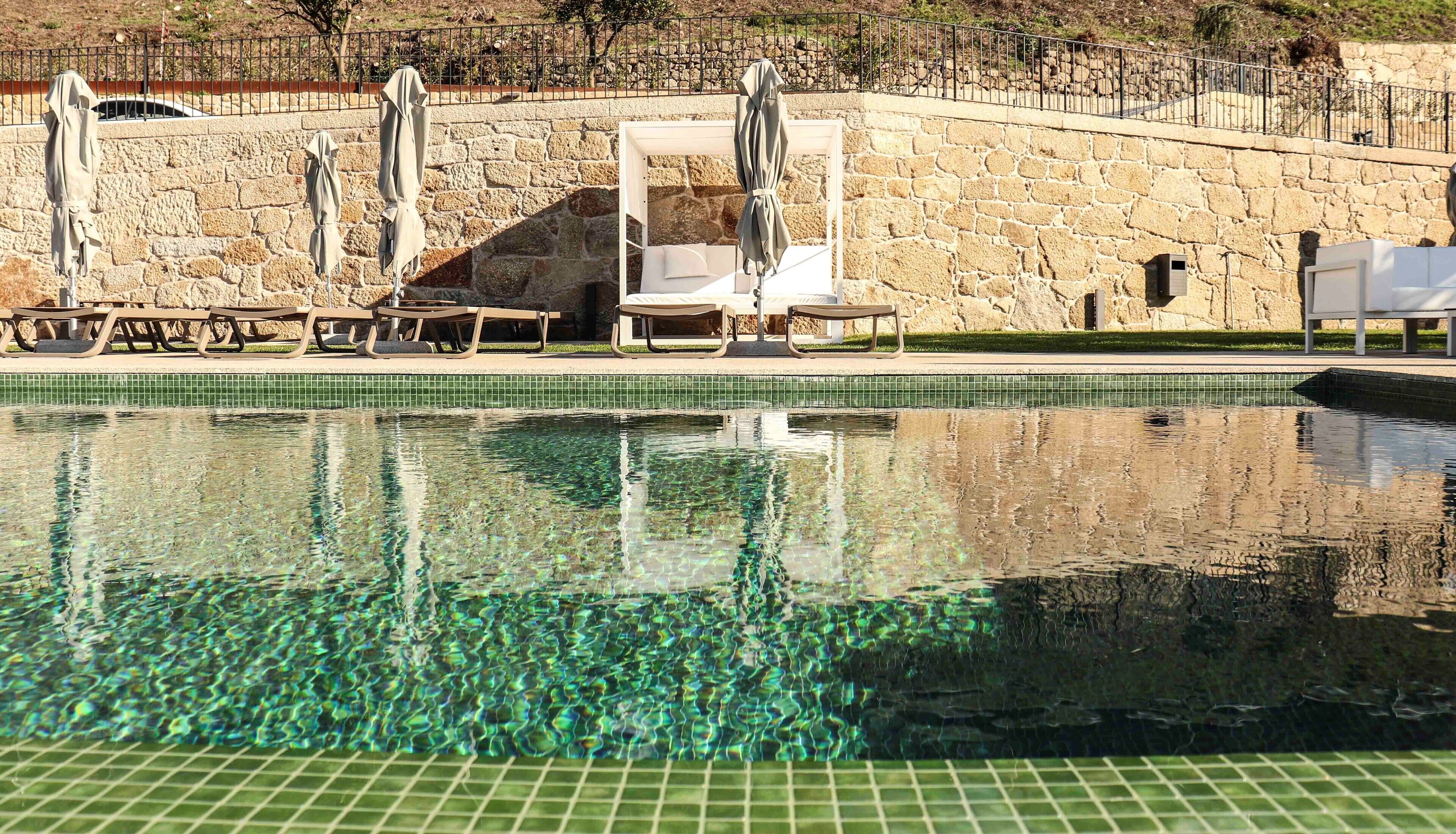 A swimming pool with clear water, surrounded by stone walls and a stone fence.