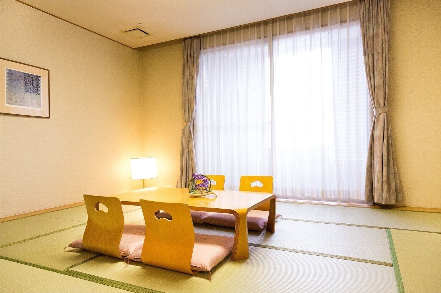 A room with tatami flooring, a wooden table with cushions, a lamp, and a window with sheer curtains.