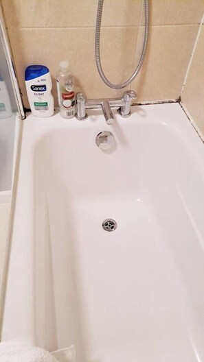 Una bañera con ducha de mano, una botella de jabón Sanex y una botella de champú.