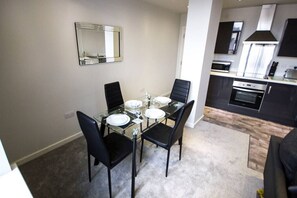 Una cocina moderna con horno empotrado y comedor con mesa de vidrio y sillas negras.