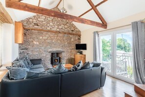 Un salón con chimenea de piedra, un sofá negro con cojines estampados y un televisor.