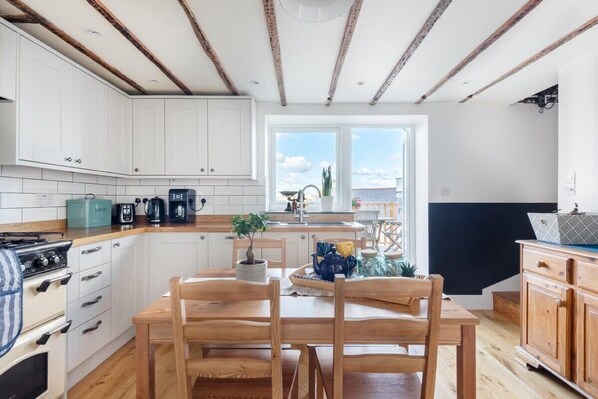 Una cucina moderna con mobili bianchi, un tavolo da pranzo in legno e vista sul mare attraverso un'ampia finestra.