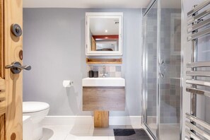 Een moderne badkamer met een toilet, een wastafel met spiegel erboven en een douchehoek.