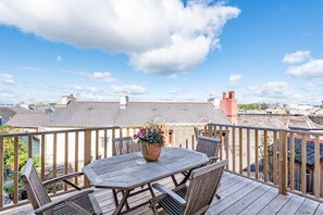 Een houten terras met een tafel en stoelen, met uitzicht op een stadsgezicht.