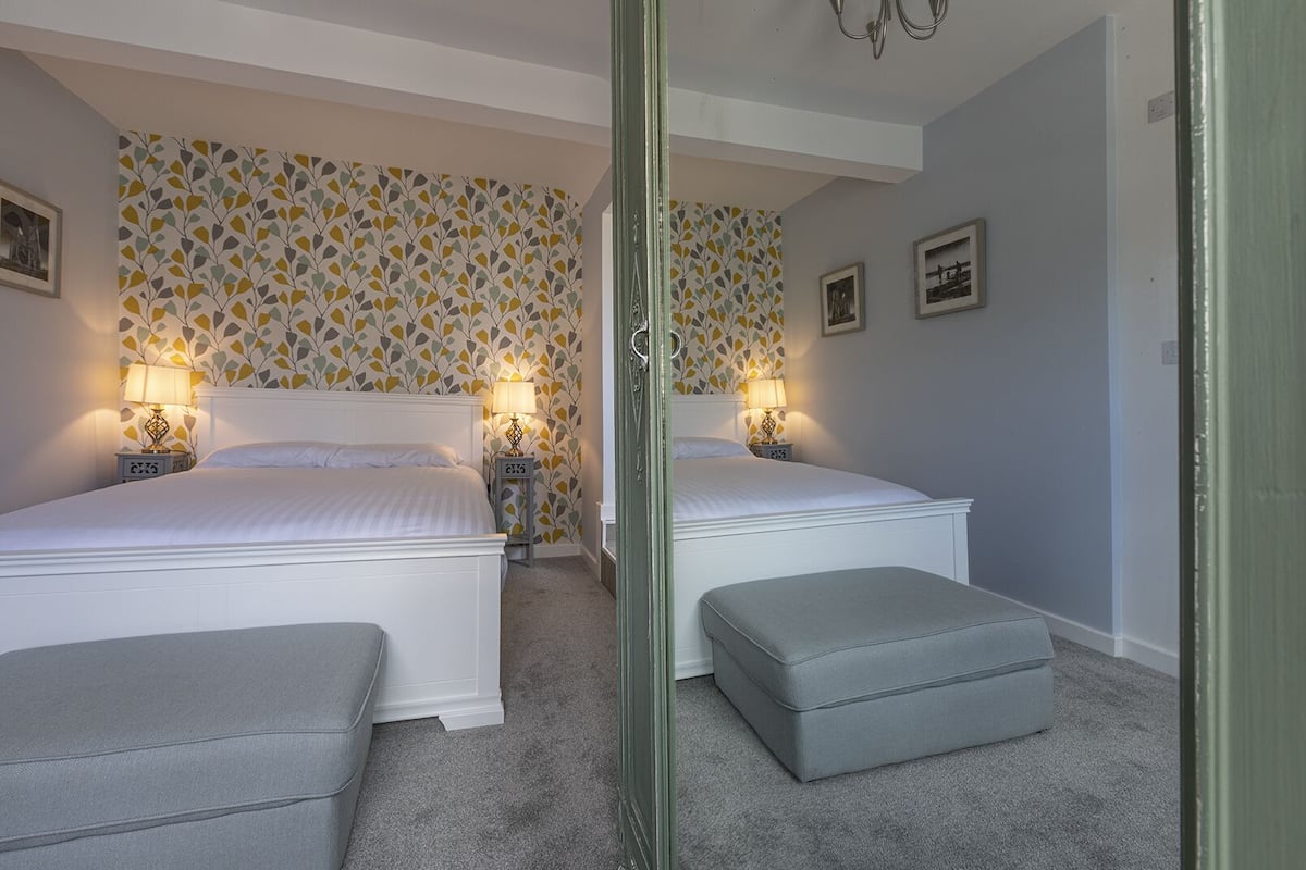A bedroom with two beds, a mirror, and a grey ottoman.
