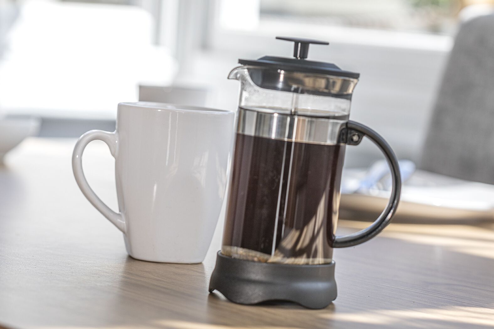 A French press coffee maker and a white mug on a wooden table.