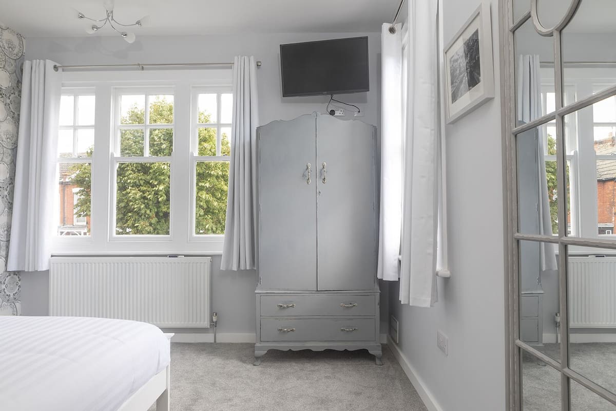 A bedroom with a bed, a wardrobe, a television, and a window with curtains.