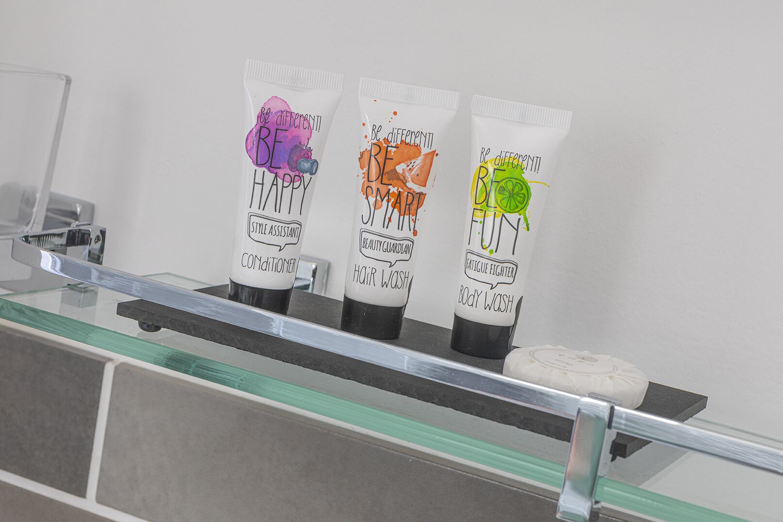 Tres botellas de jabón de baño sobre un estante de vidrio en un baño.