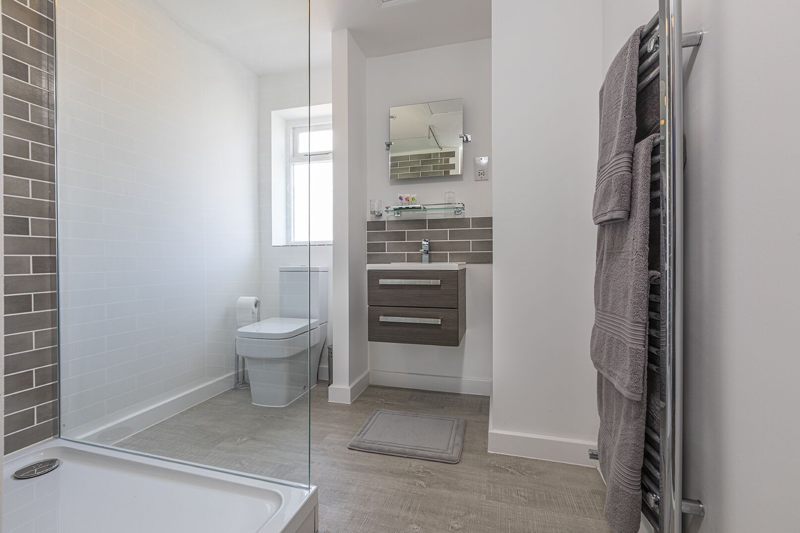 Une salle de bain moderne avec une douche à parois de verre, des toilettes, un meuble-lavabo avec un miroir et un porte-serviettes.