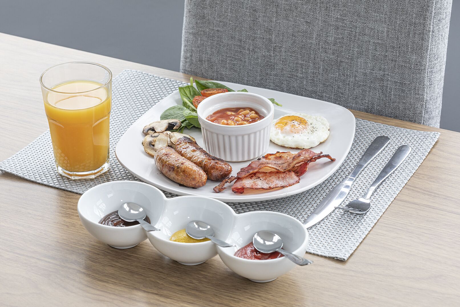 A breakfast plate with sausages, bacon, a fried egg, and a glass of orange juice.