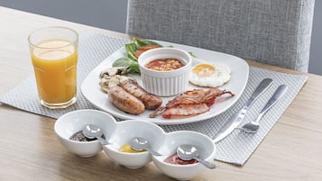 A breakfast plate with sausages, bacon, a fried egg, and a glass of orange juice.