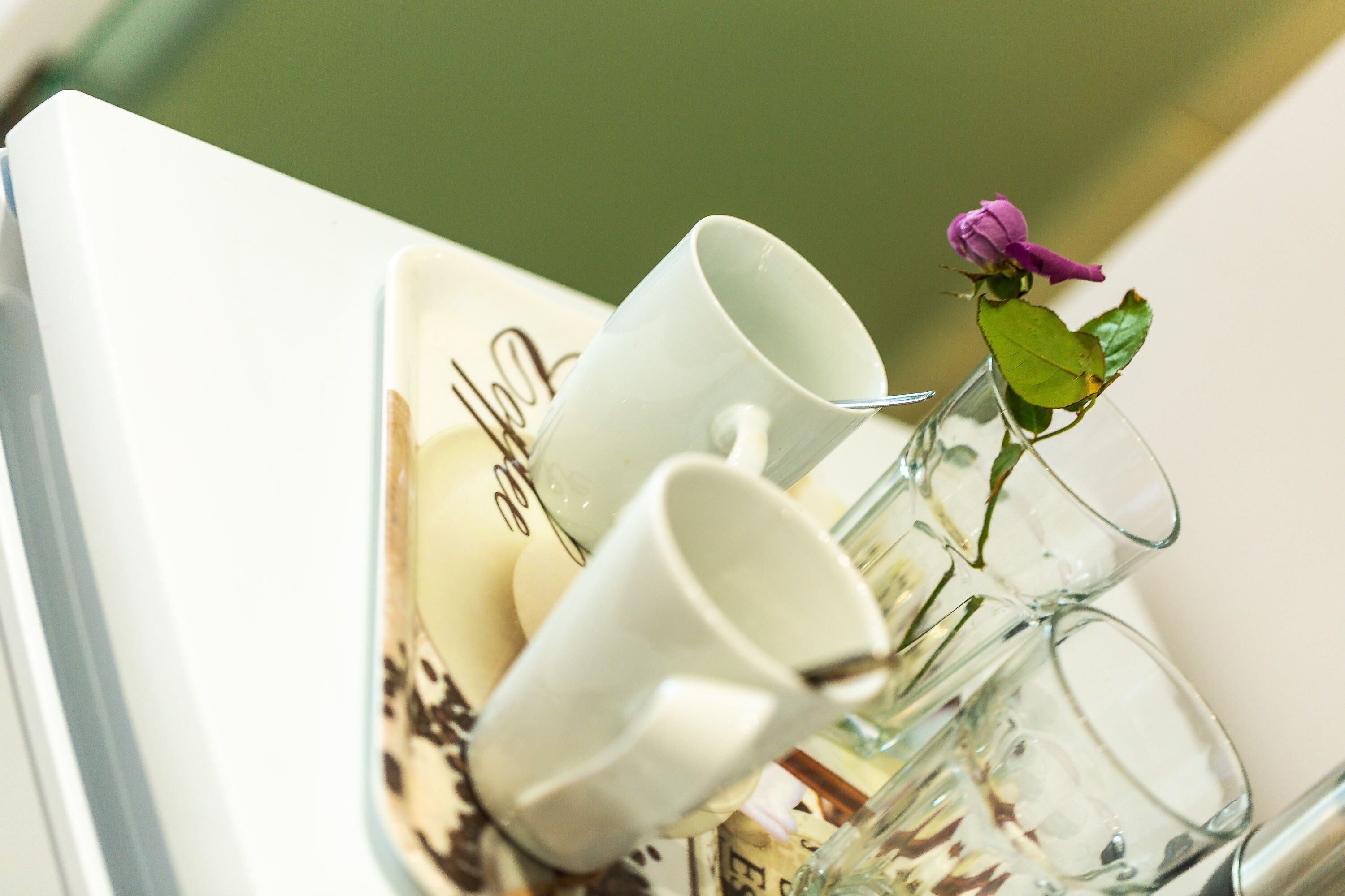 Un plateau sur lequel reposent trois tasses en céramique blanche et un vase en verre contenant une seule rose violette.