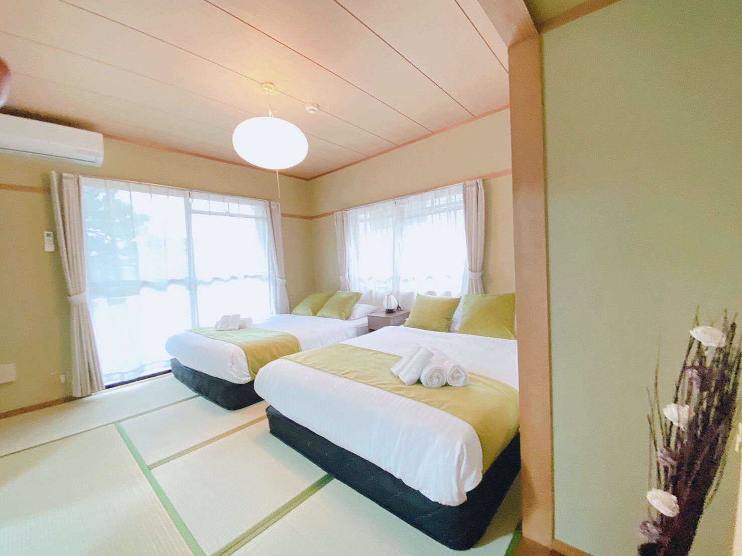 Een hotelkamer met twee bedden, een plafondventilator en uitzicht op de omgeving.