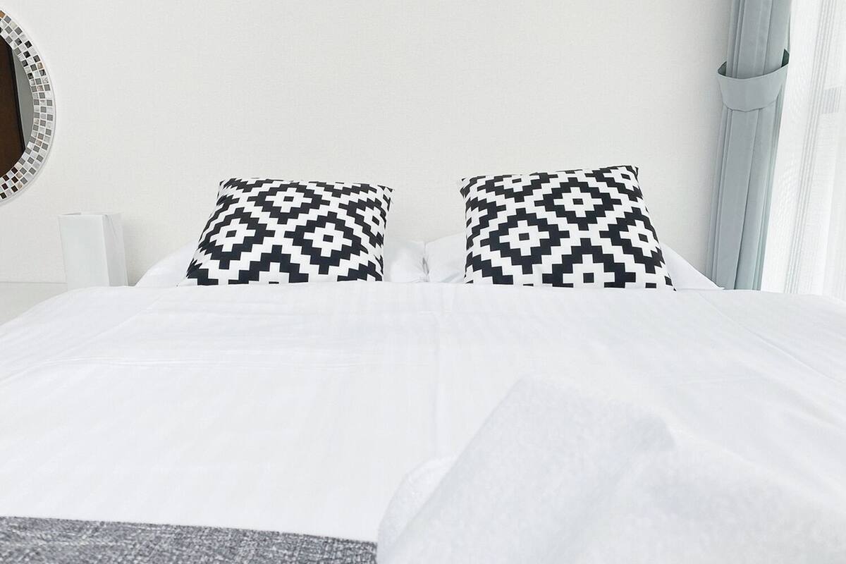 A bed with white bedding and two black and white patterned pillows.