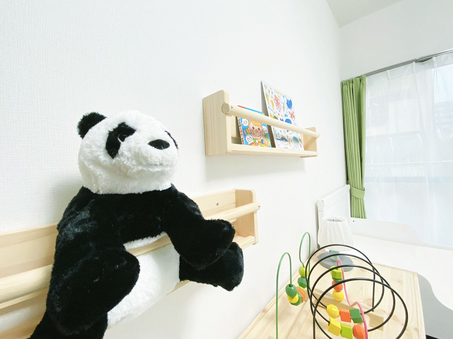 A room with a panda plush toy, a wooden shelf with children's books, and a wooden play table with a toy.
