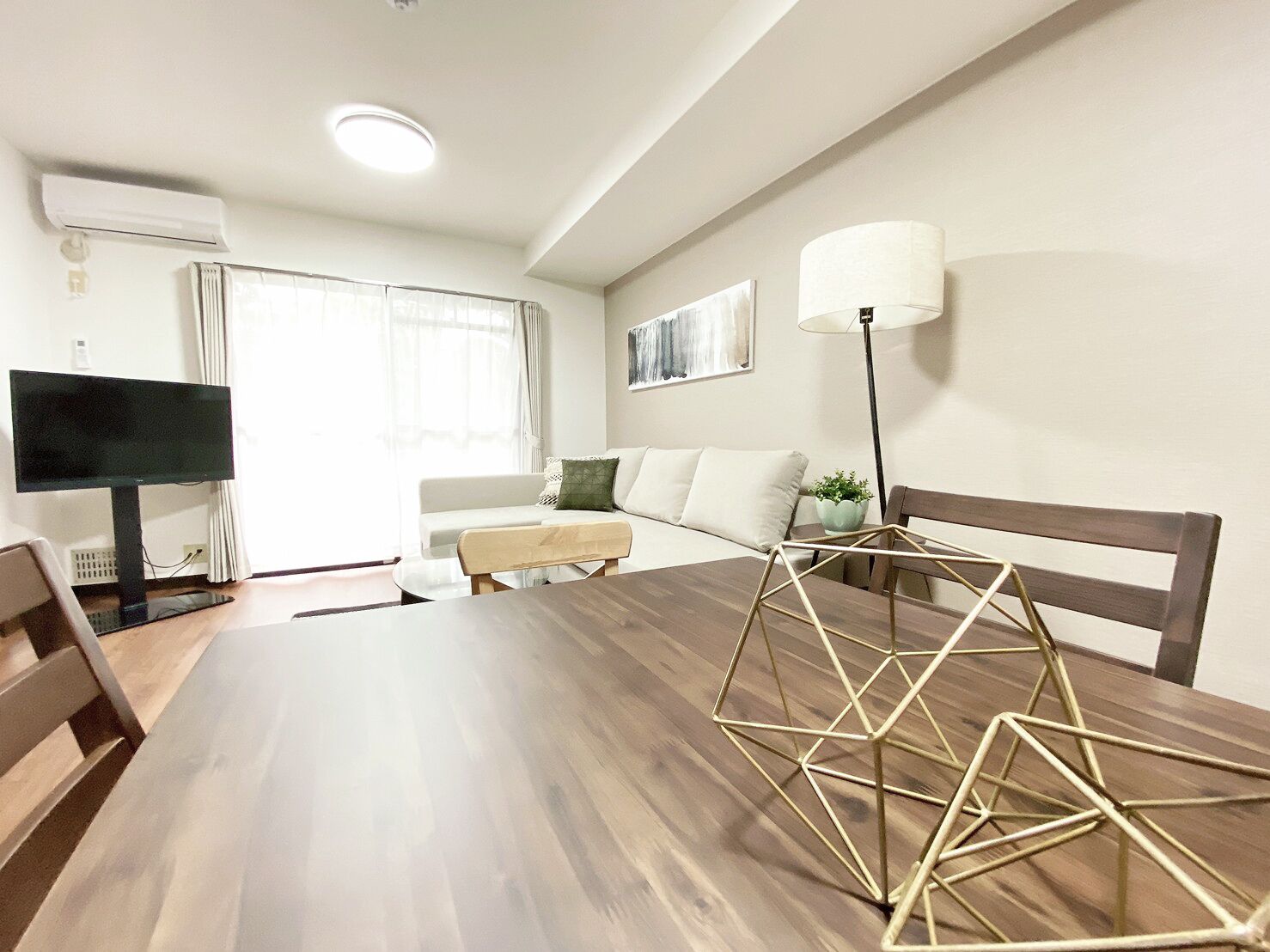 A modern living room with a wooden dining table, a sofa, a TV, and a lamp.