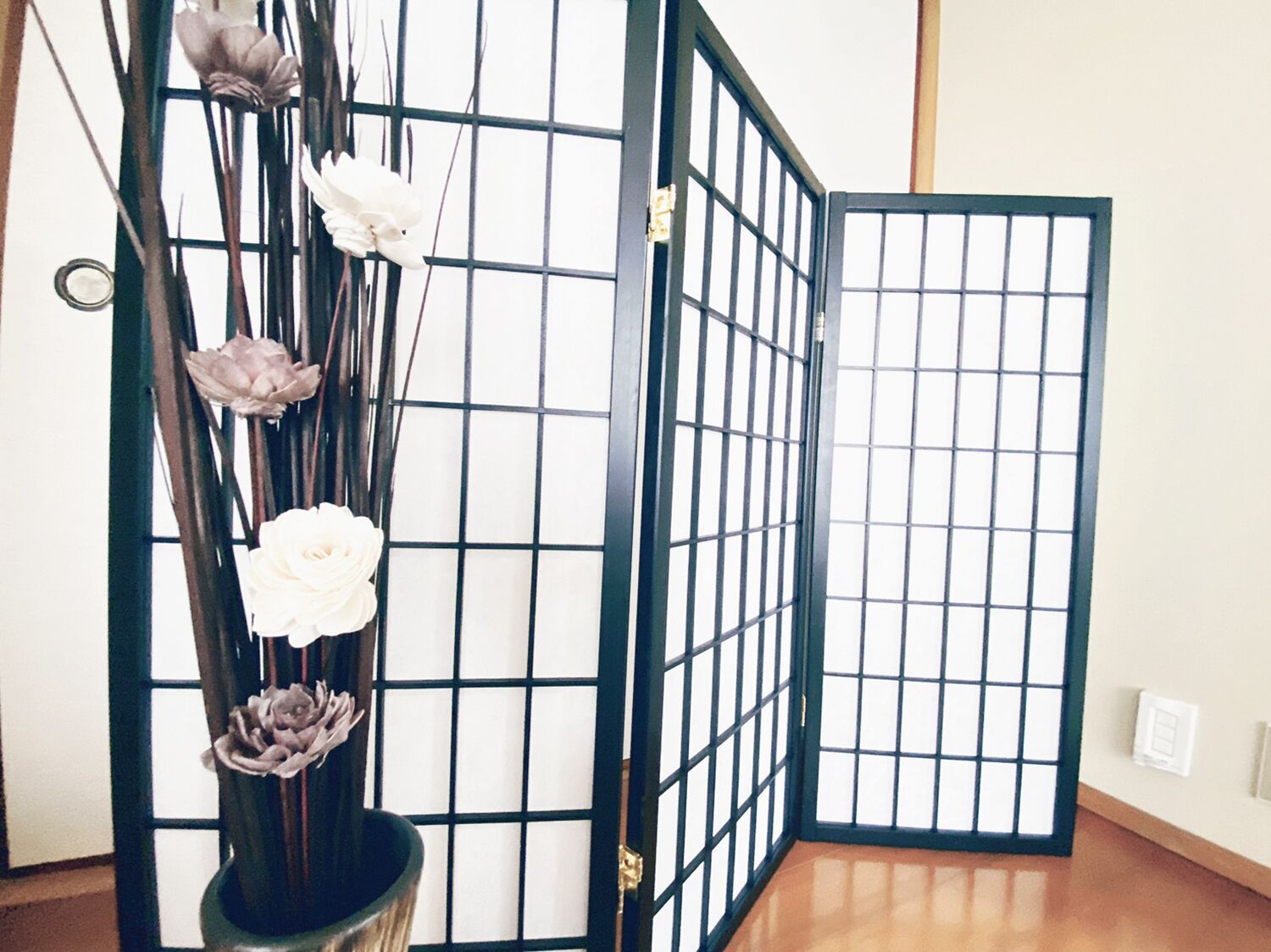 Une pièce dotée d’une porte coulissante de type shoji, d’un plancher en bois et d’un vase contenant des fleurs blanches.