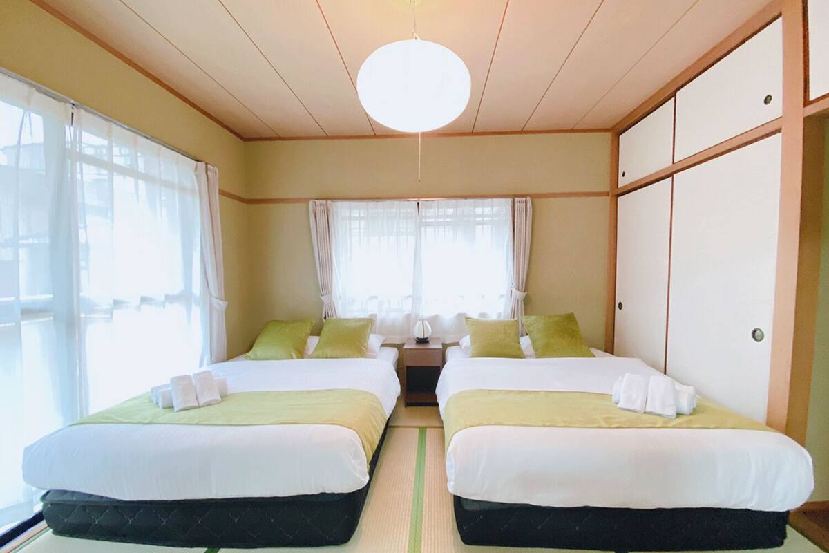 A hotel room with two beds, a large window with curtains, a ceiling light, and a wardrobe.