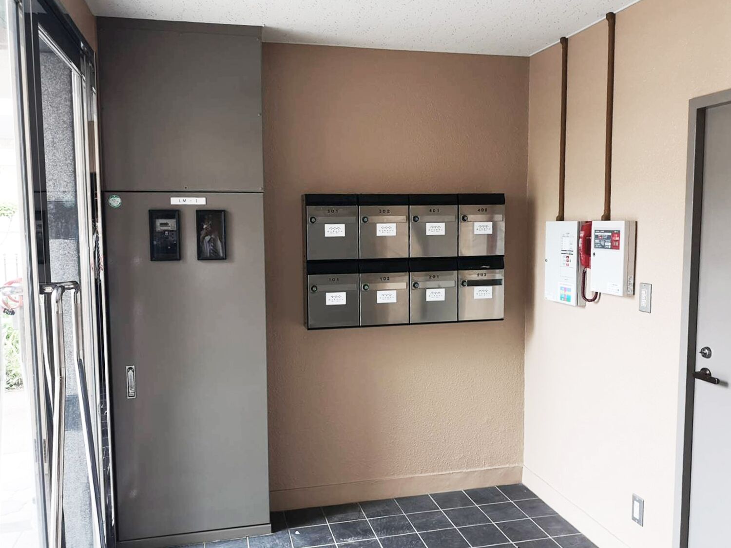 A hallway with a metallic refrigerator, a mail slot, and a fire alarm on the wall.