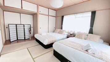 A traditional Japanese-style bedroom with tatami flooring, two beds with white bedding, a shoji screen, and a hanging paper lantern.