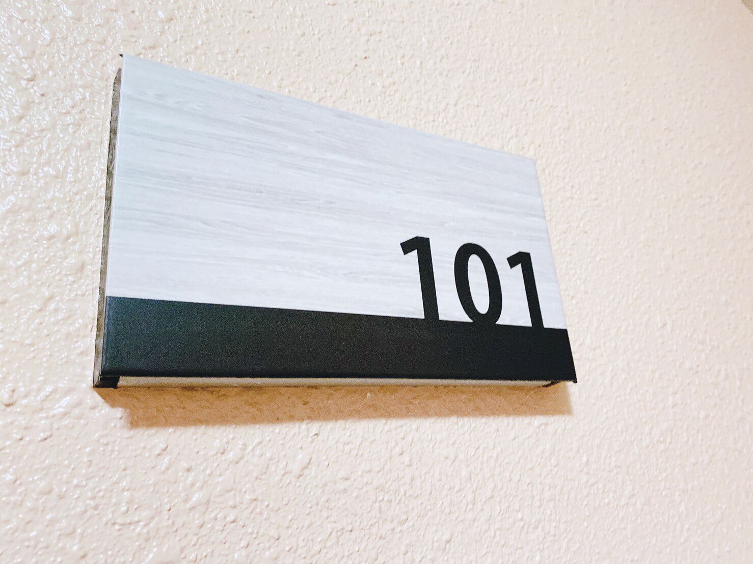 A wooden sign with the number 101 on a textured wall.