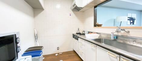 A compact kitchen with white cabinets, a stainless steel sink, a microwave, and a stove.