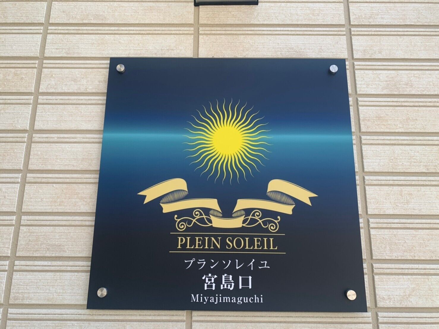 Un senyal amb el text "PLEIN SOLEIL" i "Miyajimaguchi" sobre un fons fosc, amb un sol i cintes.
