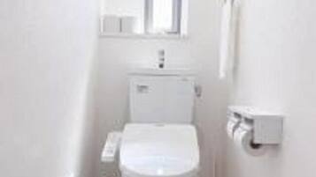 A small, white bathroom with a toilet, a window above the sink, and a towel dispenser on the wall.